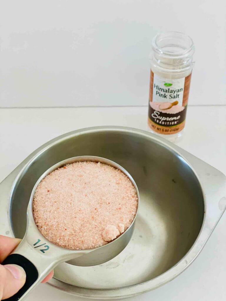 Measure out your pink sea salt to make make your own salt scrub. Image of someone measuring sea salt.