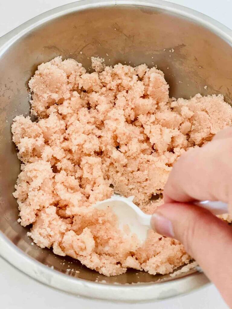 Using a spoon, mix up this coconut salt scrub. Image of someone stirring up a DIY salt body scrub.