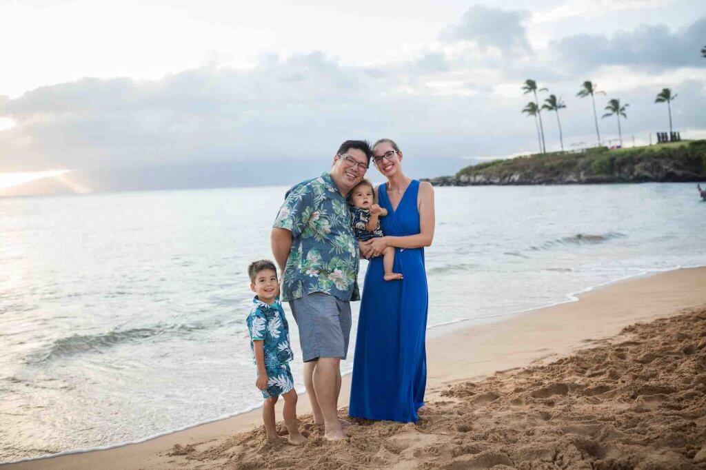 One of the best things to do in Maui with kids is do a professional photo shoot. Image of a family posing on the beach in Maui.