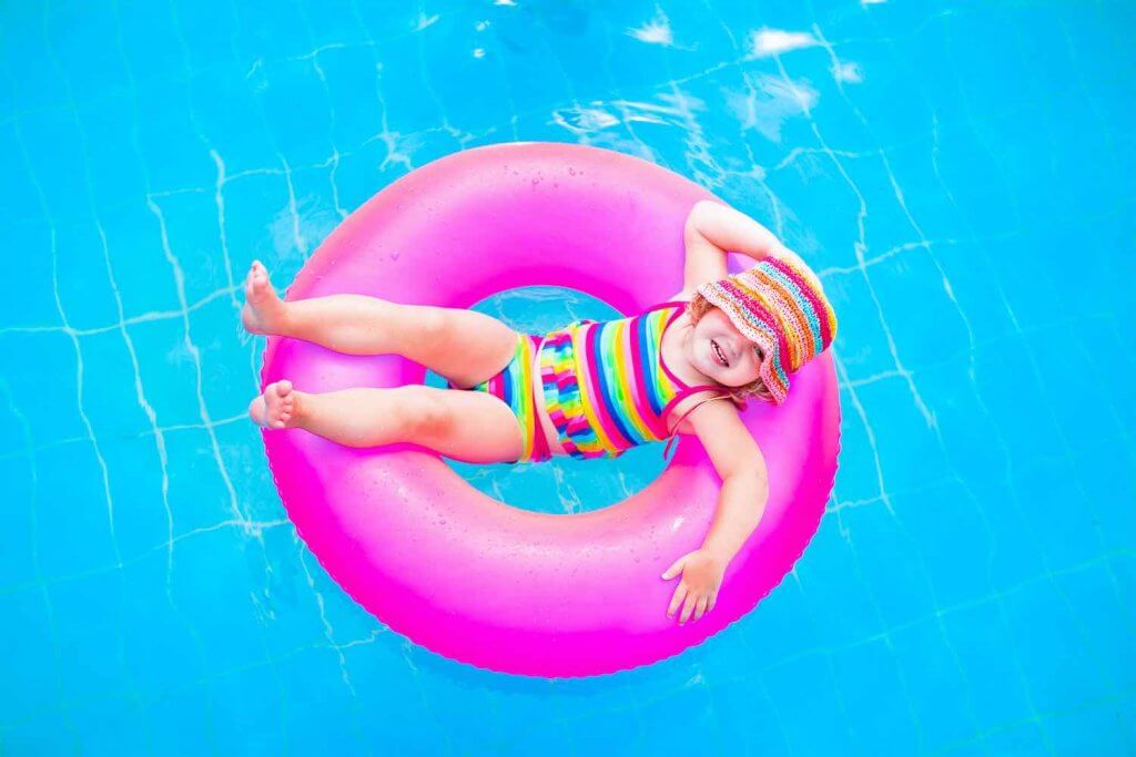 One of the top things to do in Maui with kids is play at the pool! Image of Cute funny little toddler girl in a colorful swimming suit and hat relaxing on an inflatable toy ring floating in a pool having fun during summer vacation in a tropical resort