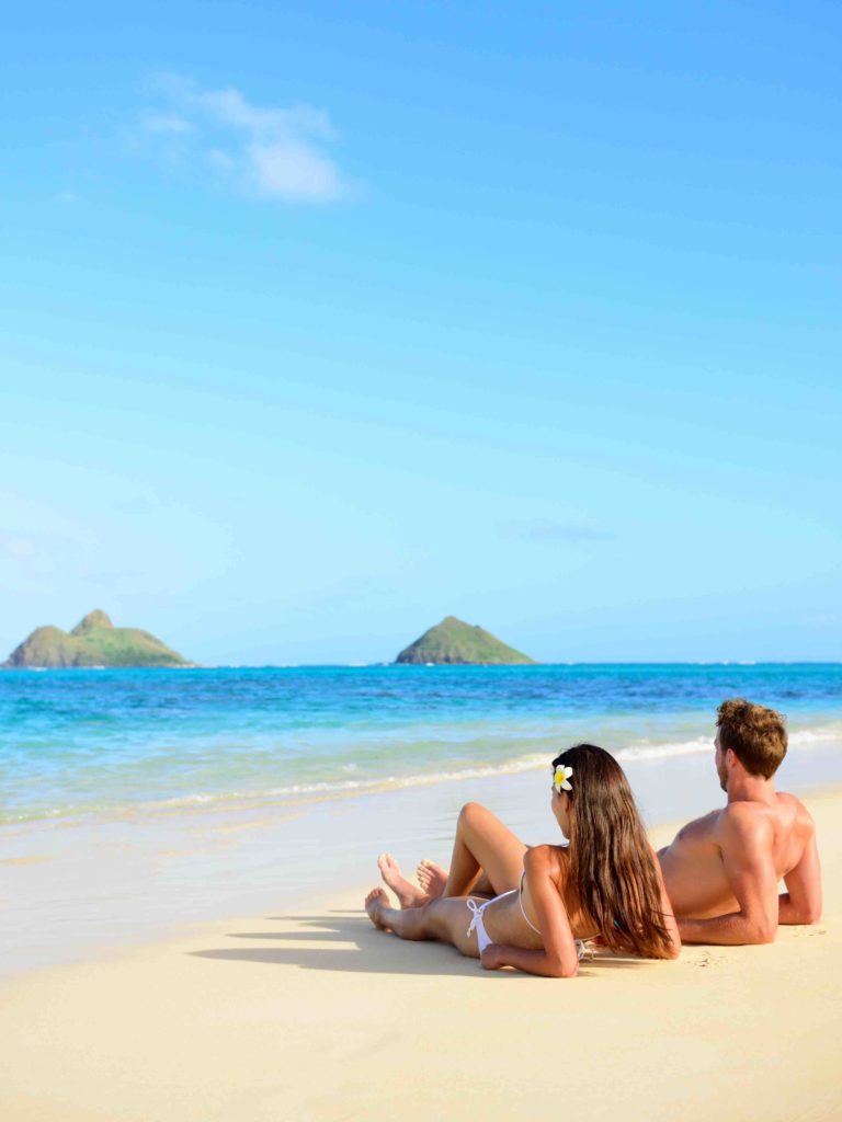 Image of Beach vacations suntan couple relaxing in Lanikai, Oahu, Hawaii, USA. Vertical crop with blue sky copy space background for holiday vacation travel concept.