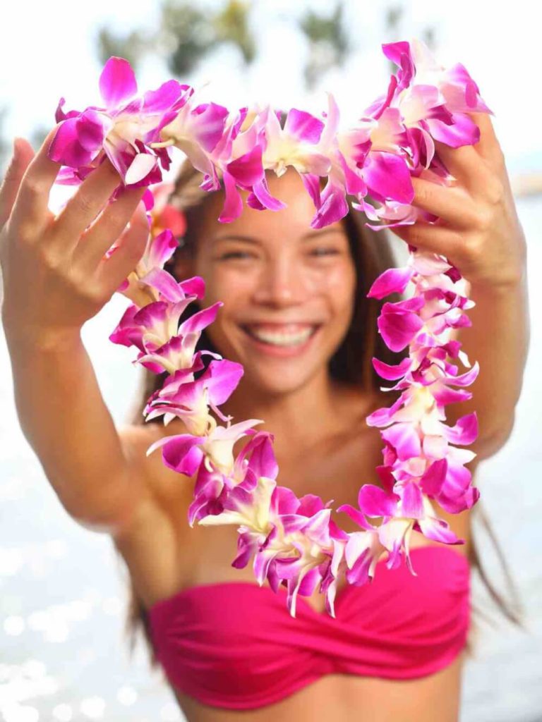 Image of Hawaii woman showing flower lei garland of pink orchids. Beautiful smiling mixed race woman in bikini on beach giving a welcoming Lei on the hawaiian island Big Island.