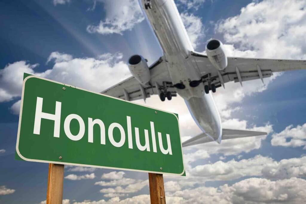 Check online for the best Hawaii flight deals. Image of Honolulu Green Road Sign and Airplane Above with Dramatic Blue Sky and Clouds.