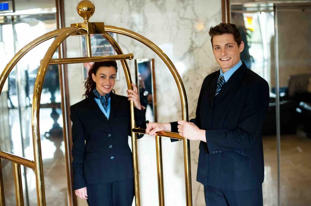 Tipping in Hawaii can be tricky. Find out how much to tip the bellhop in Hawaii. Image of two bellhops with a luggage cart.