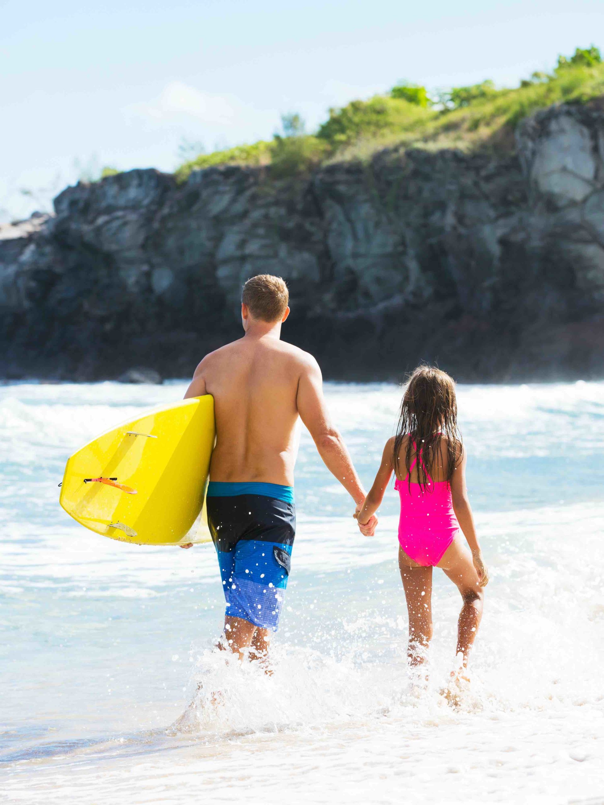 Find out all the best things to do in Kauai with kids by top Hawaii blog Hawaii Travel with Kids. Image of a father and daughter wearing swimsuits and walking in the ocean in Hawaii.