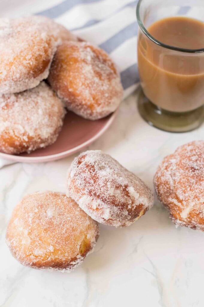 Get this Hawaiian malasada recipe by top Hawaii blog Hawaii Travel with Kids. Image of a bunch of sugar coated malasadas with a cup of coffee.