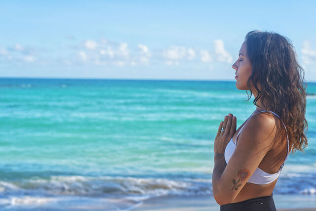 Image of a woman meditating while doing Maui beach yoga.