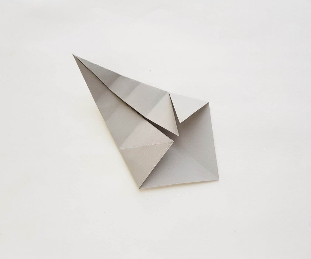 See how to make a paper shark craft. Image of a grey paper folded and unfolded a bunch of times.