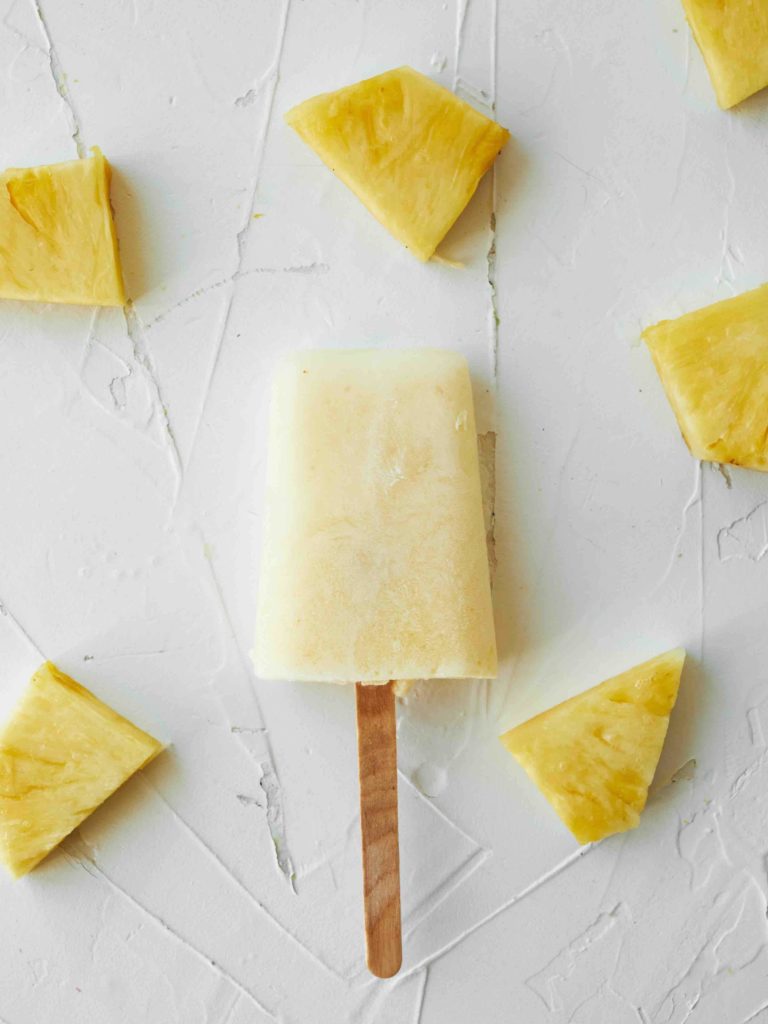 Learn how to make homemade pineapple popiscles by top Hawaii blog Hawaii Travel with Kids. Image of a frozen pineapple popsicle surrounded by pineapple chunks.