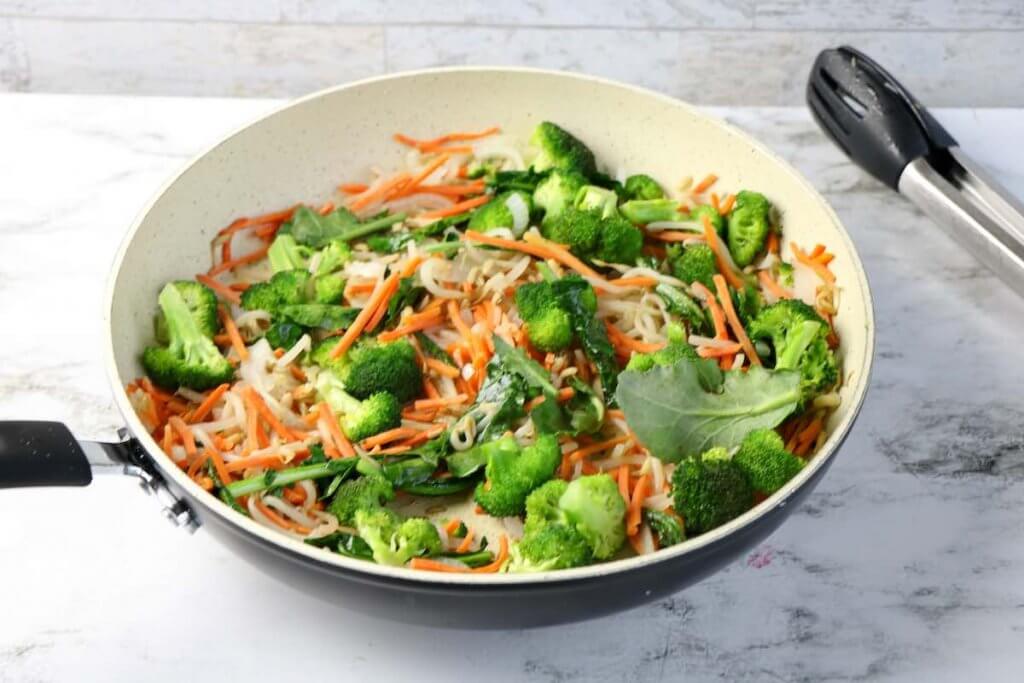 Stir fry the vegetables in a pan. Image of chopped broccoli, carrots, and bean sprouts in a skillet.