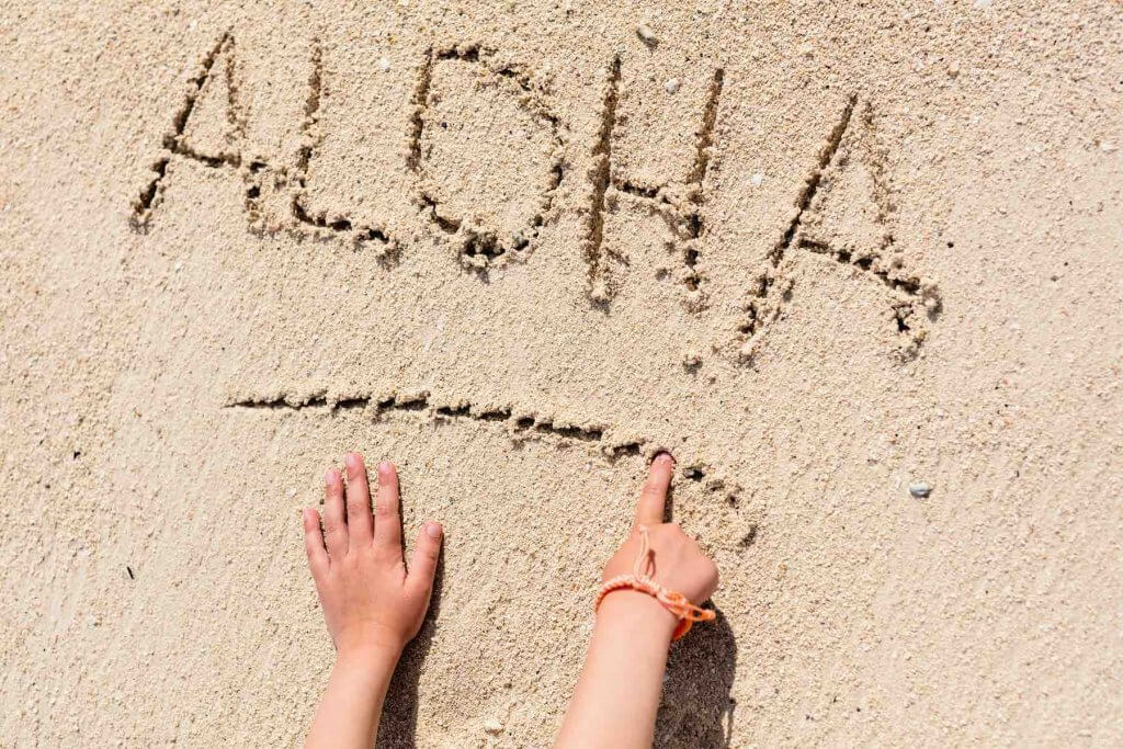 It's helpful to learn a few words in the Hawaiian language before your trip. Image of the word "aloha" written in the sand.