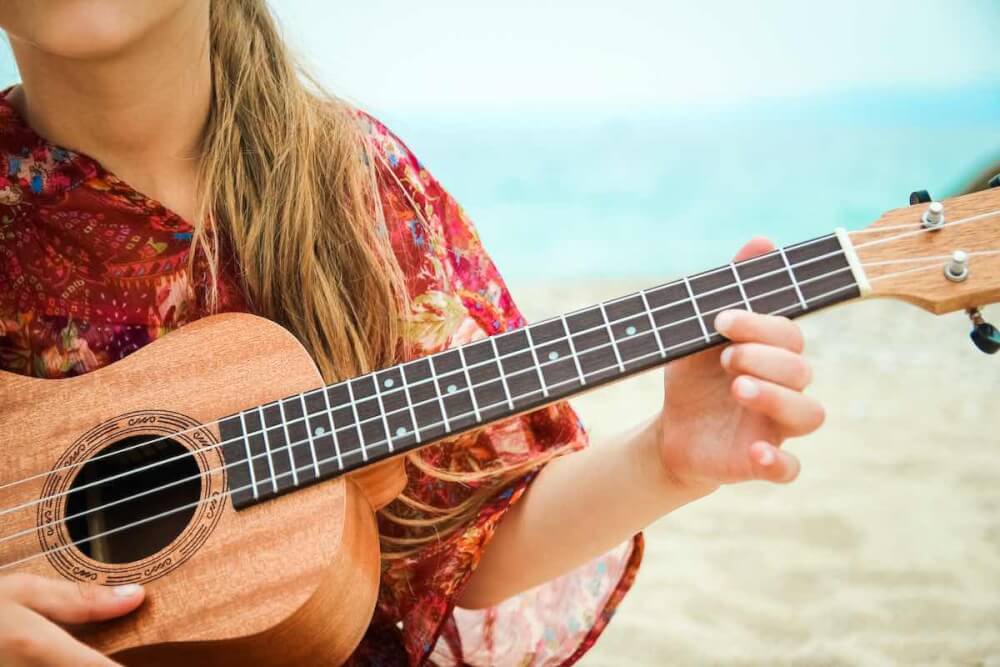 Find out the most famous Hawaiian songs by top Hawaii blog Hawaii Travel with Kids. Image of a child playing the ukulele on the beach.