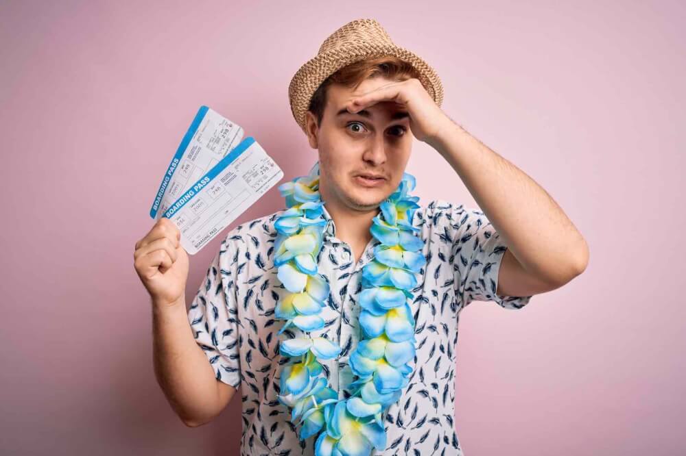 Find out the top Hawaii mistakes tourists make from top Hawaii blog Hawaii Travel with Kids. Image of a redhead tourist man on vacation wearing hawaiian lei holding boarding pass and looking stressed out.