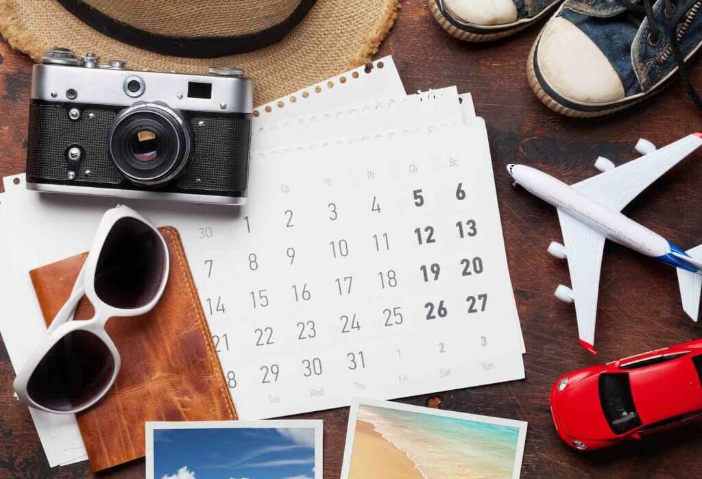 Find out how to plan a trip to Hawaii by top Hawaii blog Hawaii Travel with Kids. Image of travel vacation concept with sun hat, camera, passport, airplane toy and weekend photos on wooden backdrop. Top view. Flat lay.