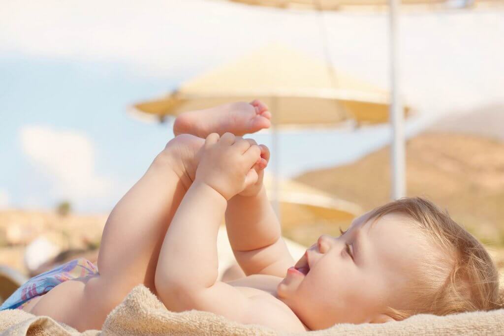 Where should you stay in Hawaii with a baby? Image of Happy baby on the beach. 8 month old kid lying on a sun lounger and playing with her feet.