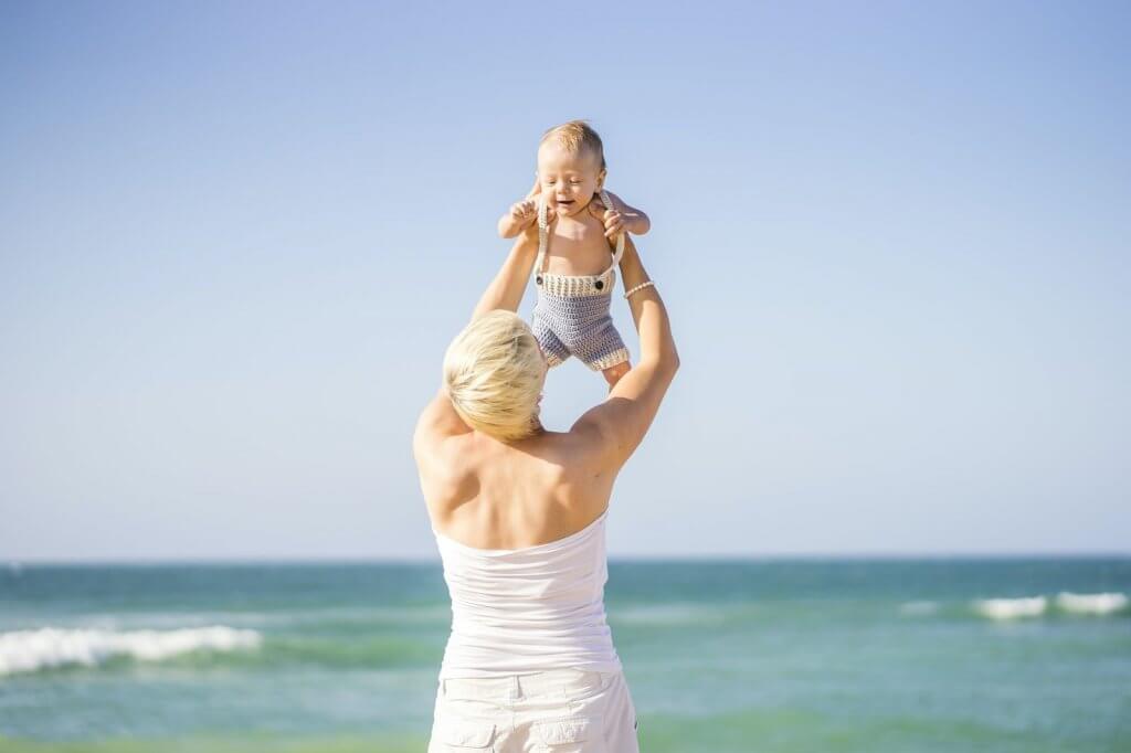 Find out why you should visit Hawaii with a baby. Image of attractive blond mother playing with 4 months old baby boy on the beach