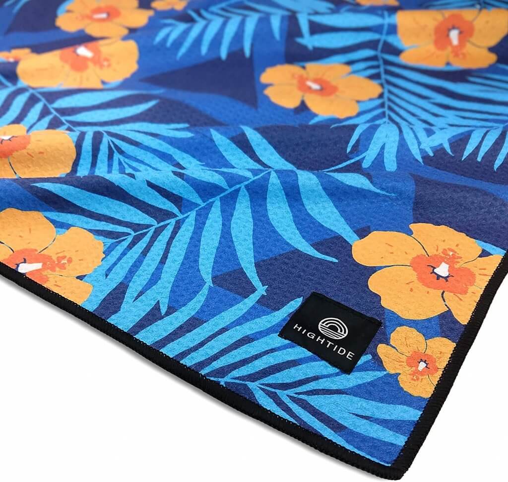 This sandfree beach towel is super handy for traveling to Hawaii with a baby. Image of a orange and blue tropical print towel.