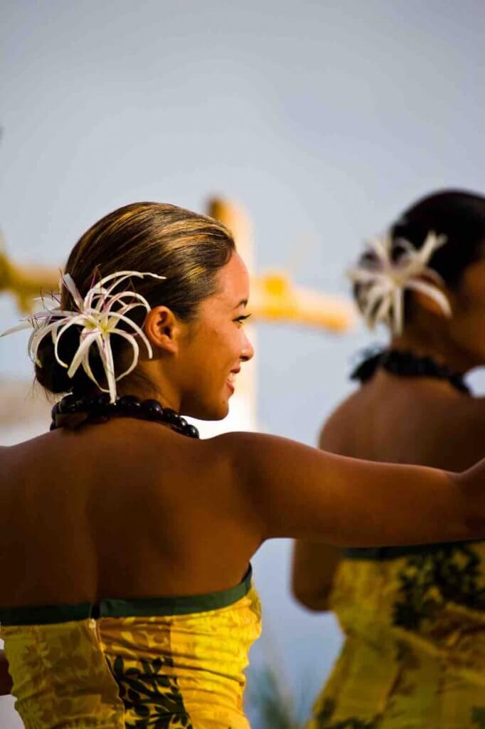  Bild einer Frau, die ein gelbes hawaiianisches Kleid und eine große weiße Blume in ihrem Haar trägt.