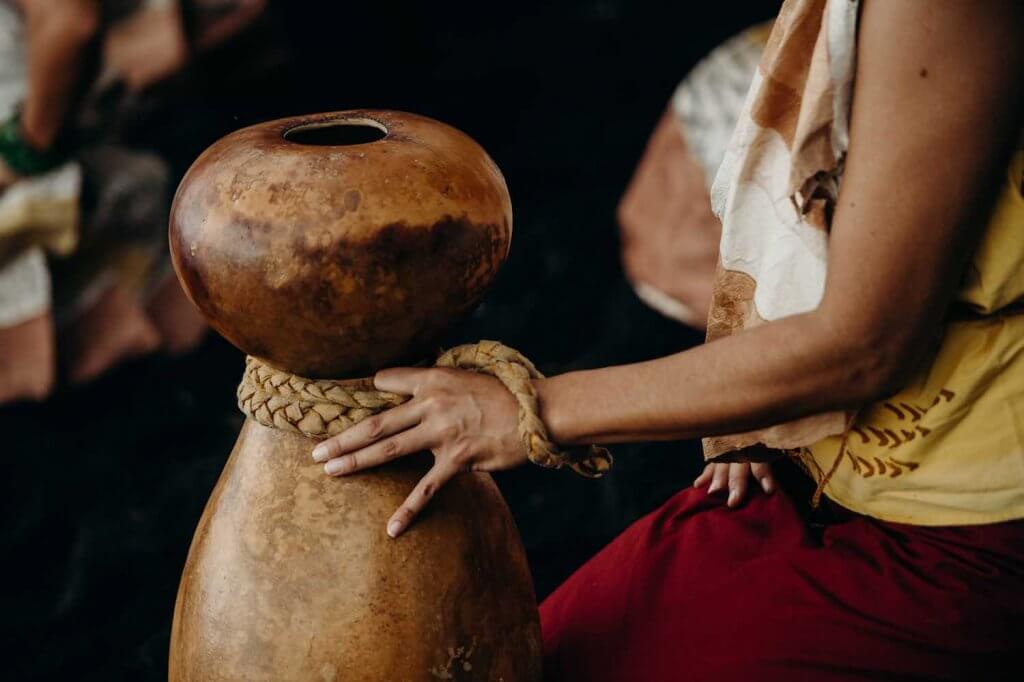 Image of a woman playing traditional Hawaiian music with an ipu heke (double gourd drum.)
