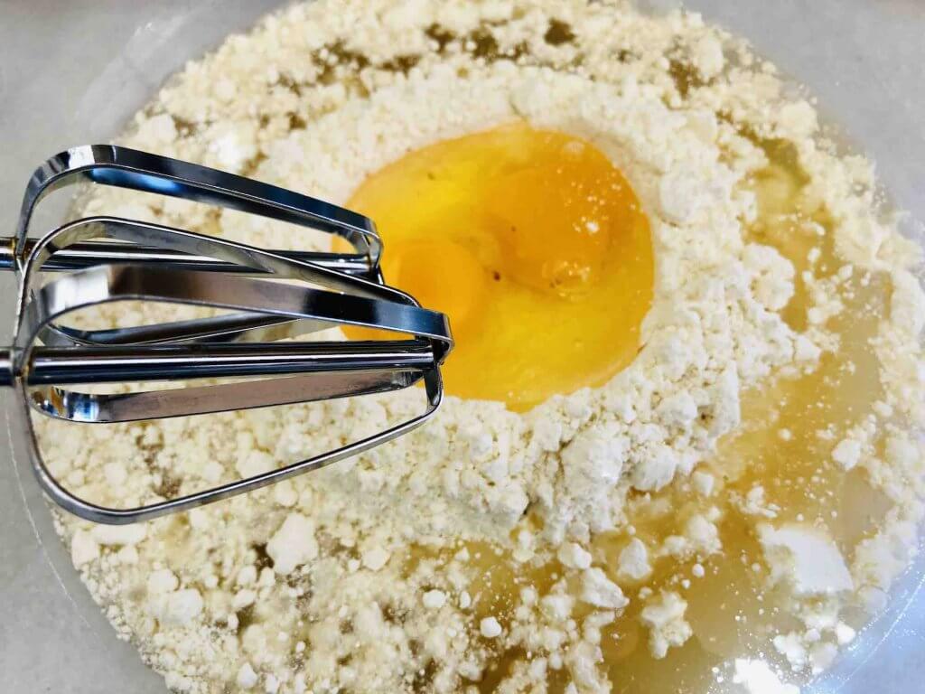 Mix up your cake mix batter and substitute pineapple juice for the water. Image of an electric mixer and a bowl full of dry cake mix, egg, and pineapple juice.