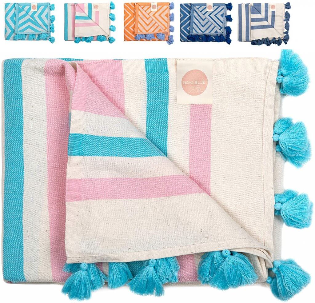 These adorable Turkish towels are some of the best baby gear for the beach. Image of a pink and blue striped Turkish towel with blue tassels on it. 