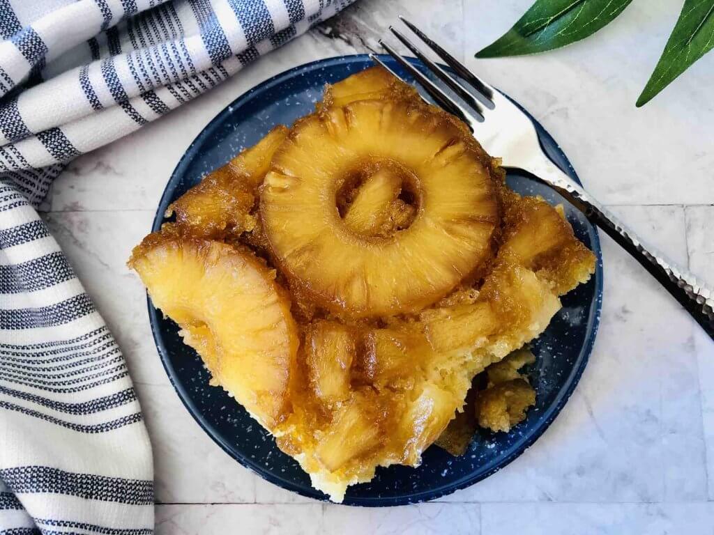 Learn how to make pineapple upside down rum cake, one of the most popular Hawaiian dessert recipes by top Hawaii blog Hawaii Travel with Kids. Image of a square piece of pineapple upside down cake on a plate with a fork.