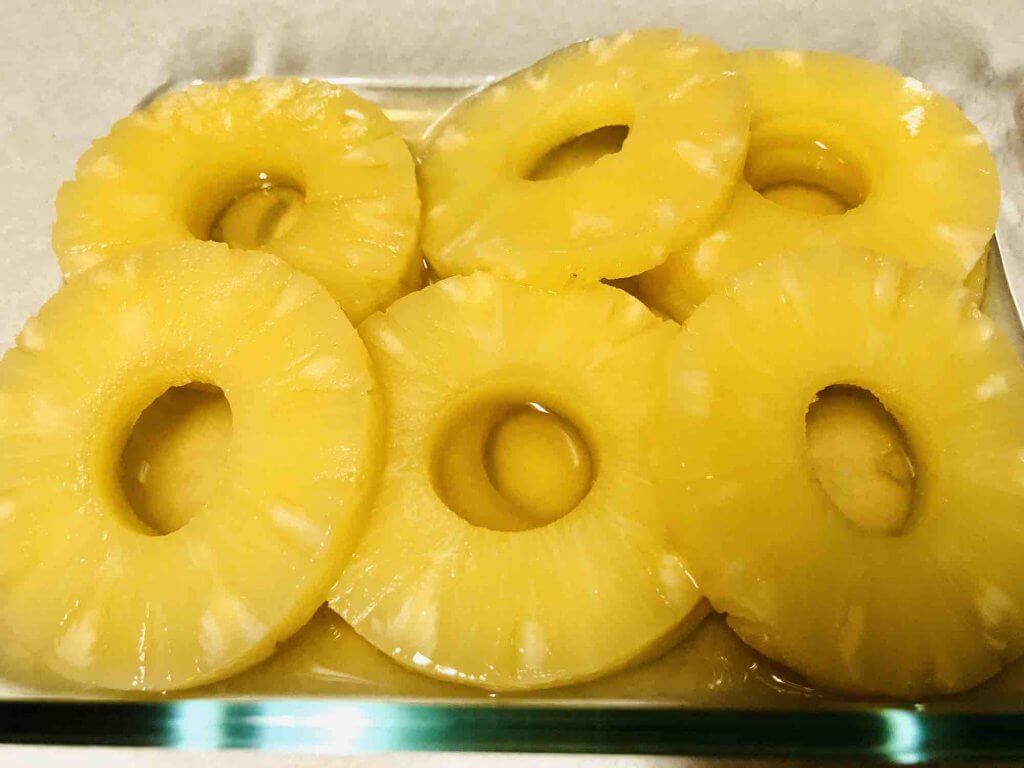 Image of pineapple rings in a pan soaking in rum.