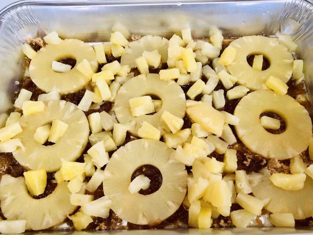 Learn how to make rum soaked pineapple upside down cake by top Hawaii blog Hawaii Travel with Kids. Image of a metal pan with pineapple rings and tidbits sprinkled inside.