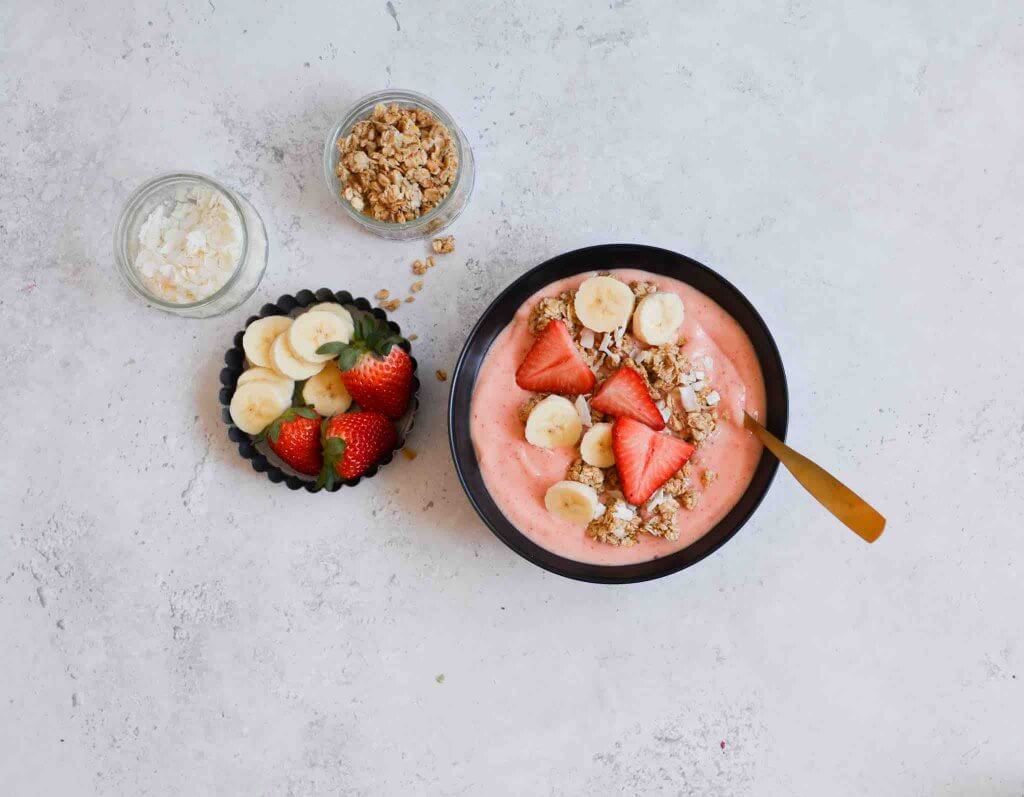 Add your favorite toppings to this mango strawberry smoothie bowl. Image of a tropical smoothie bowl with small bowls of fresh fruit, coconut flakes, and granola.