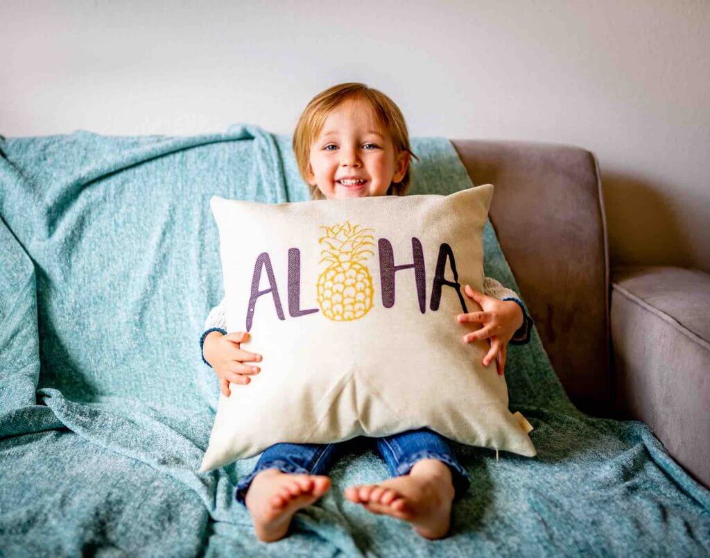 Find out where to stay in Hawaii with toddlers. Image of a boy holding a pillow with the word "aloha" on it.