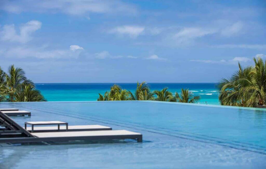 The Alohilani Resort & Spa is one of the best kid friendly hotels on Oahu. Image of an infinity pool with lounge chairs in the water and a view of the ocean.