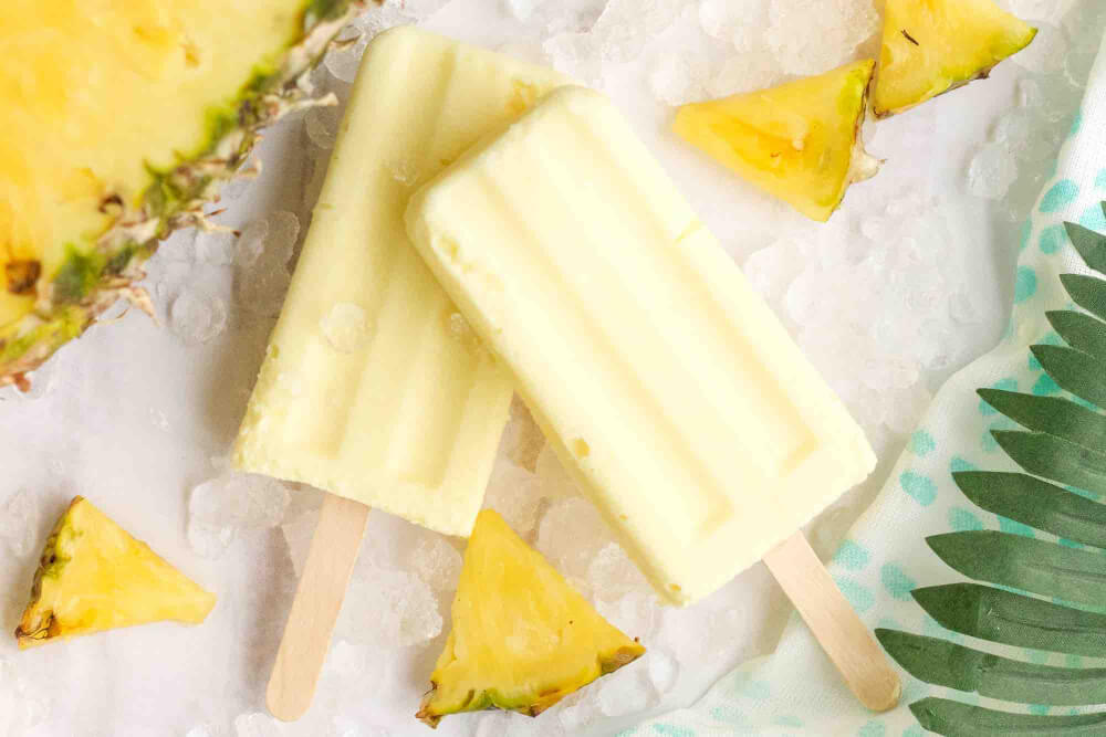 Learn how to make Dole Whip popsicles by top Hawaii blog Hawaii Travel with Kids. Image of 2 pineapple popsicles stacked next to a fresh pineapple