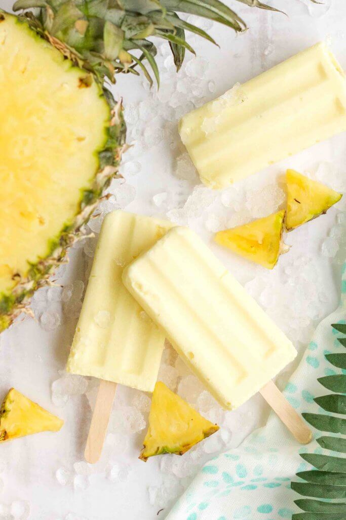 Get my Dole Whip pineapple popsicle recipe by top Hawaii blog Hawaii Travel with Kids. Image of pineapple popsicles next to a fresh pineapple