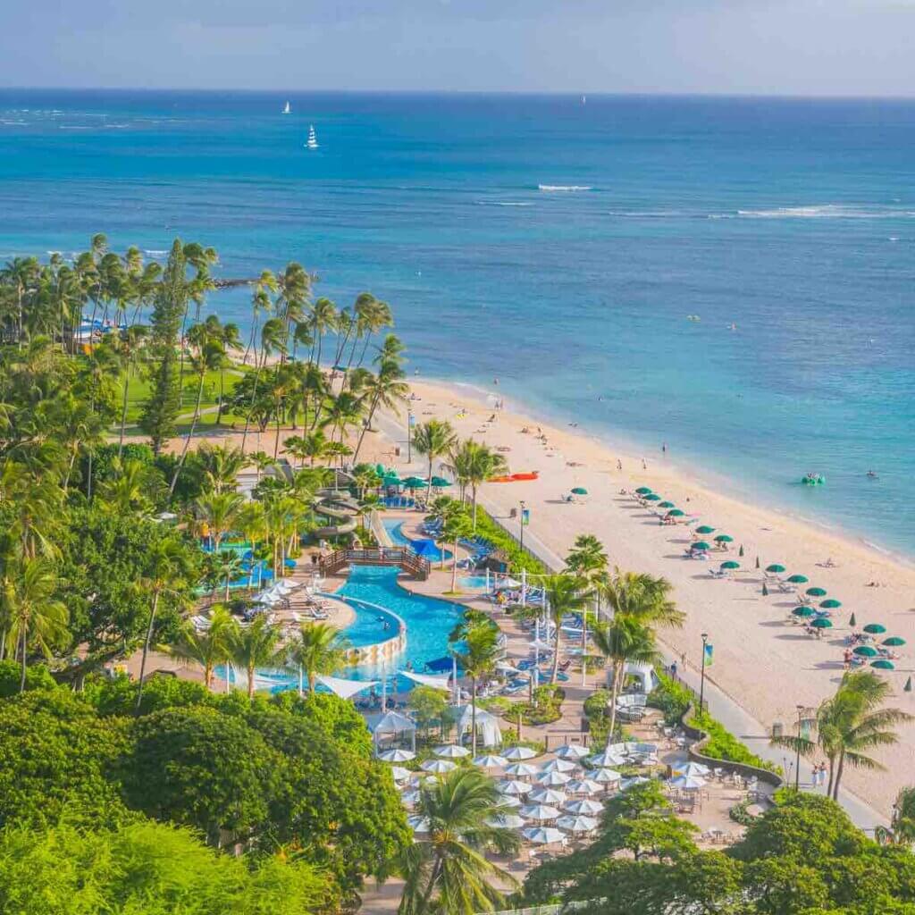 The Hale Koa is the top place to stay for a military vacation to Hawaii. Image of a beachfront hotel with pool area.