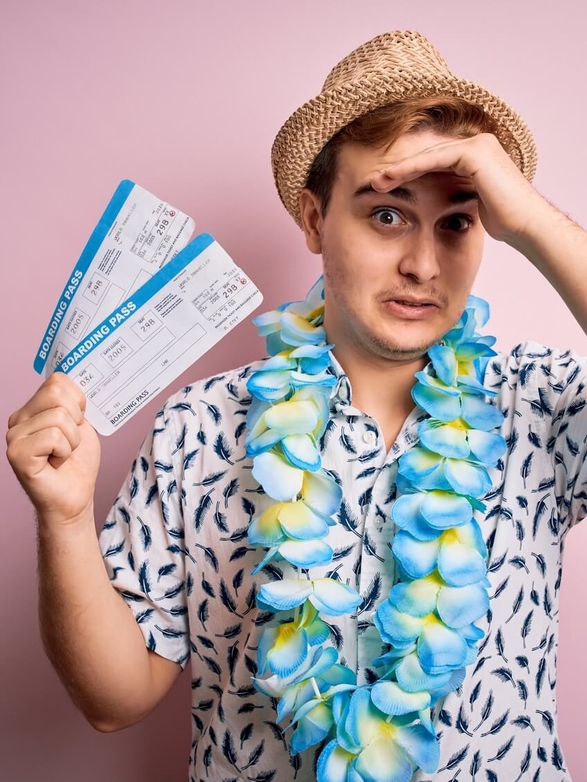 Find out the biggest Hawaii mistakes tourists make by top Hawaii blog Hawaii Travel with Kids. Image of a man wearing a Hawaiian shirt, blue lei, a straw hat, and holding airplane tickets.
