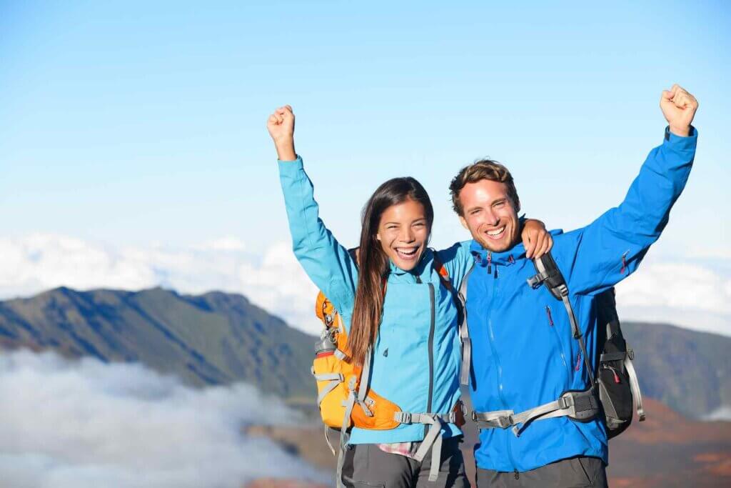 Hikers - people hiking cheering on summit top with view on volcano. Don't forget to wear warm clothes when hiking Haleakala National Park. Image of a hiker couple looking at beautiful landscape of mountain volcanoes at Haleakala on Maui.