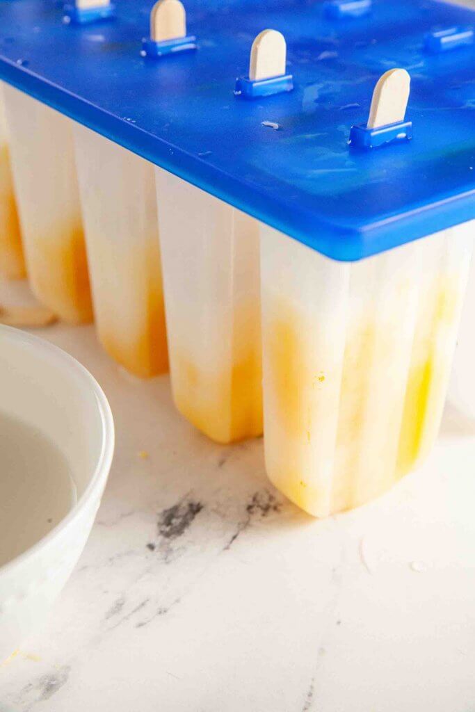 Pour the mixture into popsicle molds. Image of coconut mango popsicles inside of popsicle molds.