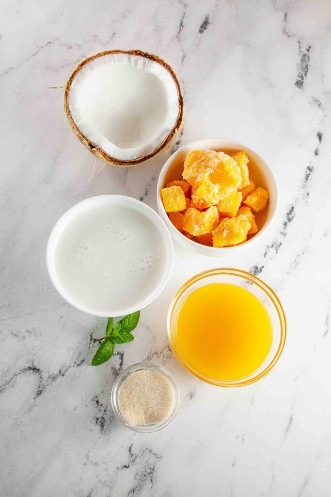 These are the ingredients to make mango coconut popsicles. Image of mango juice, frozen mango chunks, sugar, and coconut milk.