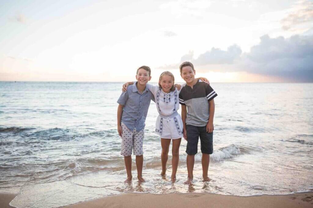 Make sure to take lots of Maui family photos with kids. Image of 3 kids posing in the water on a beach in Maui.