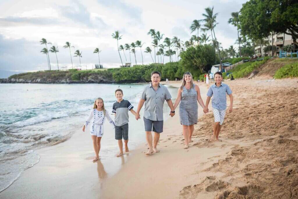 Get the cutest Maui family photos at the beach during golden hour. Image of a family of five holding hands and walking on the beach.