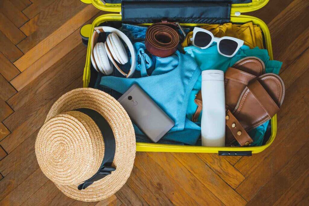 Find out what to add to your packing list for Maui by top Hawaii blog Hawaii Travel with Kids. Image of a yellow suitcase filled with items for a tropical vacation.