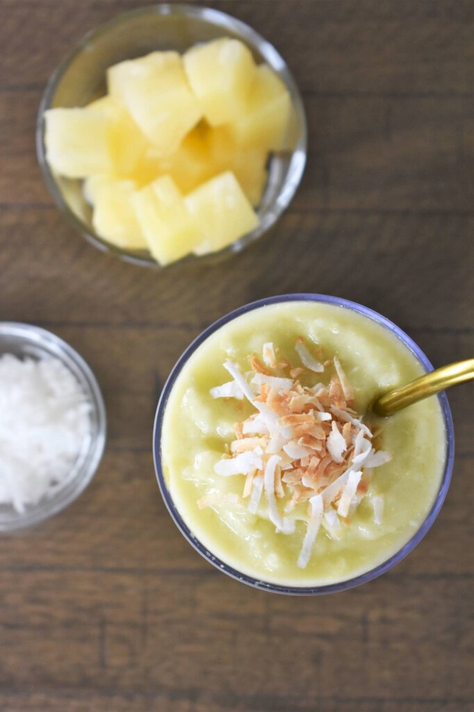 Learn how to make this avocado pineapple smoothie by top Hawaii blog Hawaii Travel with Kids. Image of an aerial shot of a pineapple coconut smoothie with avocado and a bowl of shredded coconut and pineapple chunks.