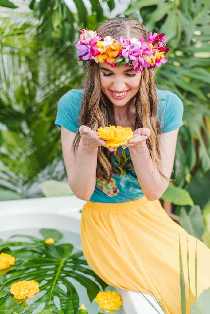 The Kauai Jungle Tub photography on Kauai includes a professional photographer who is great at giving directions. Image of a women looking down at a yellow flower as she sits at the edge of an outdoor bathtub.