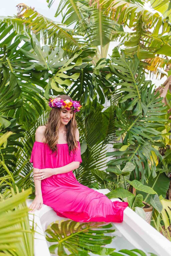 Bring lots of outfits for your photoshoot on Kauai. Image of a woman wearing a pink maxi dress as she sits at the edge of an outdoor bathtub on Kauai.