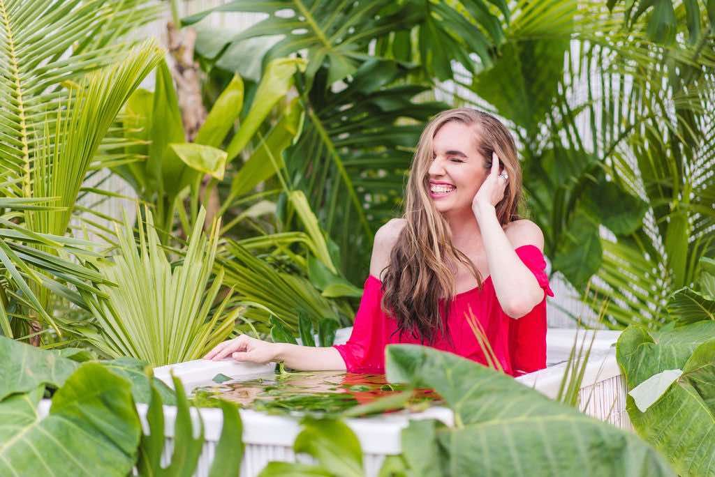 Looking for a Kauai photographer? Book a Kauai Jungle Tub photoshoot in Hawaii. Image of a woman wearing a pink dress sitting in an outdoor tropical bathtub