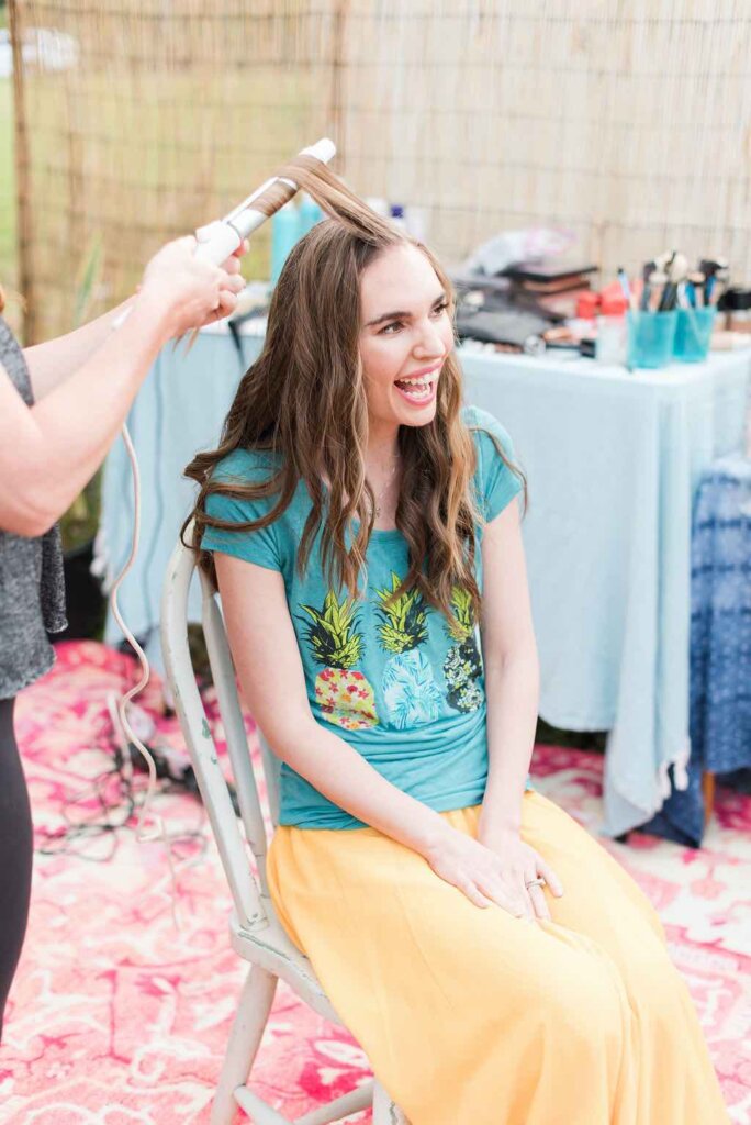 You'll get professional hair and makeup done at this Kauai photo session. Image of a woman getting her hair curled outside.