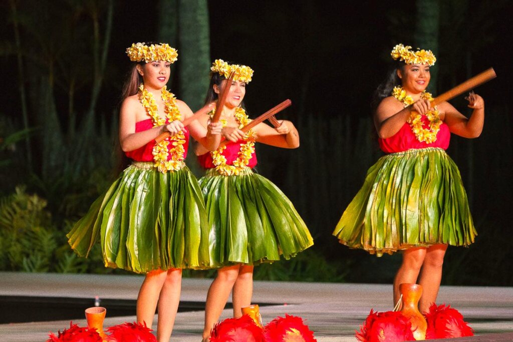 One of the best luaus on Kauai for kids is Smith Family Luau. Image of three hula dancers wearing ti leaf skirts and red tops