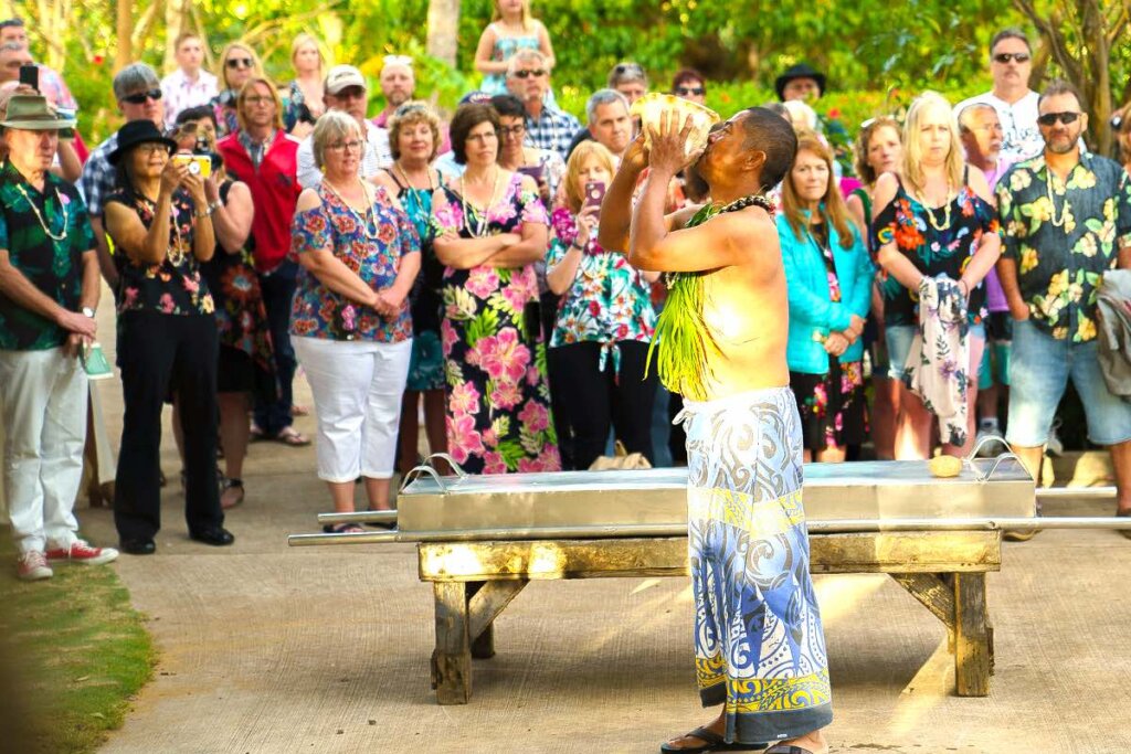 Image of a man blowing a conch shell at a Kauai luau imu ceremony.