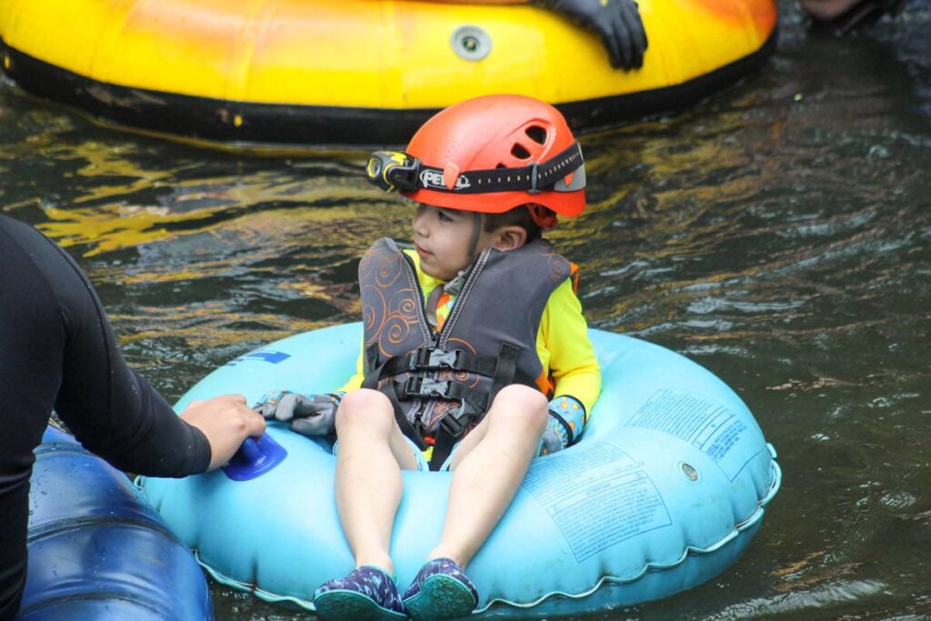 One of the best things to do with kids on Kauai is go mountain tubing. Image of a 5yo boy in a blue inner tube on the water.