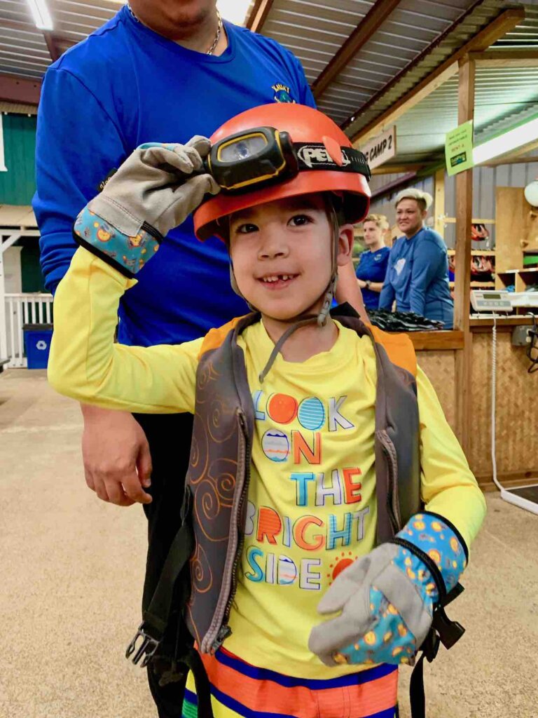 Image of a boy wearing a headlamp, rashguard, life vest, and gloves as he preps for a Kauai mountain tubing adventure.